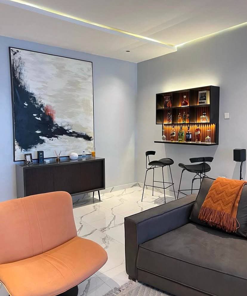 A lounge corner with a built in bar, abstract art and a burnt orange chair