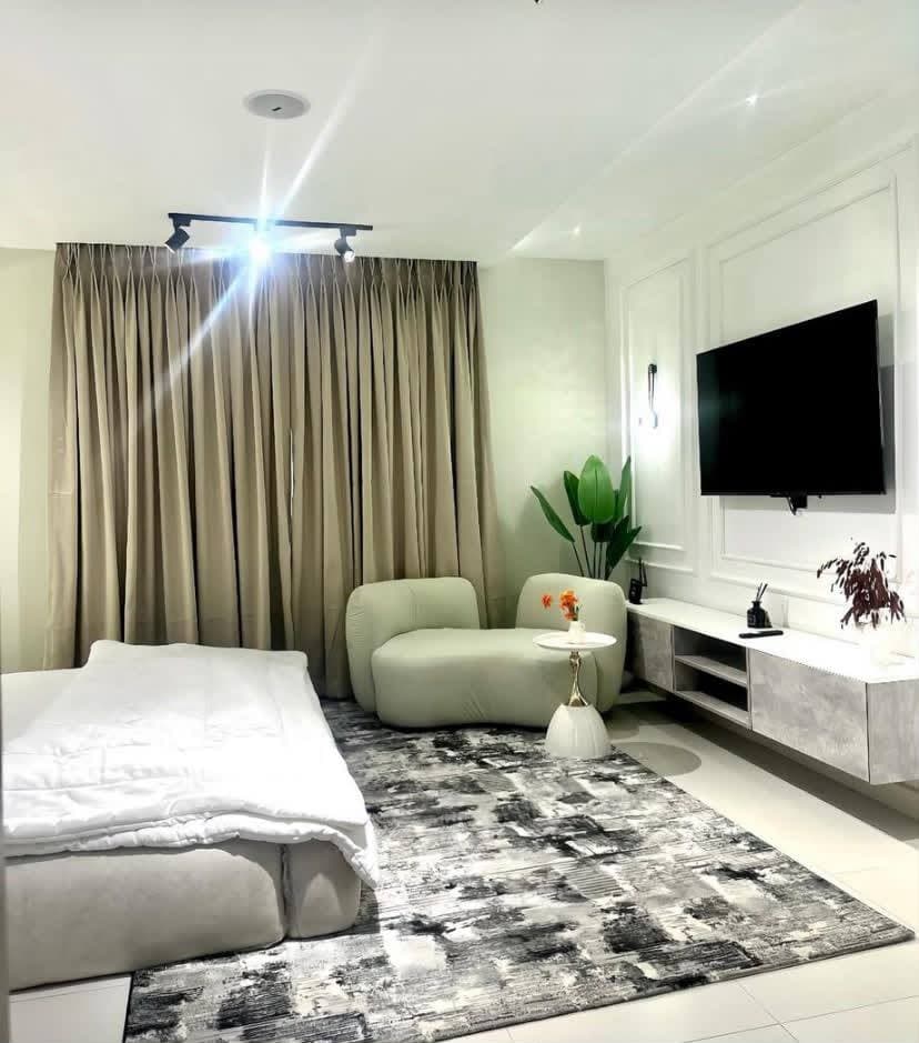 An open studio room with a bed, a curved lounge sofa and a wall mounted television