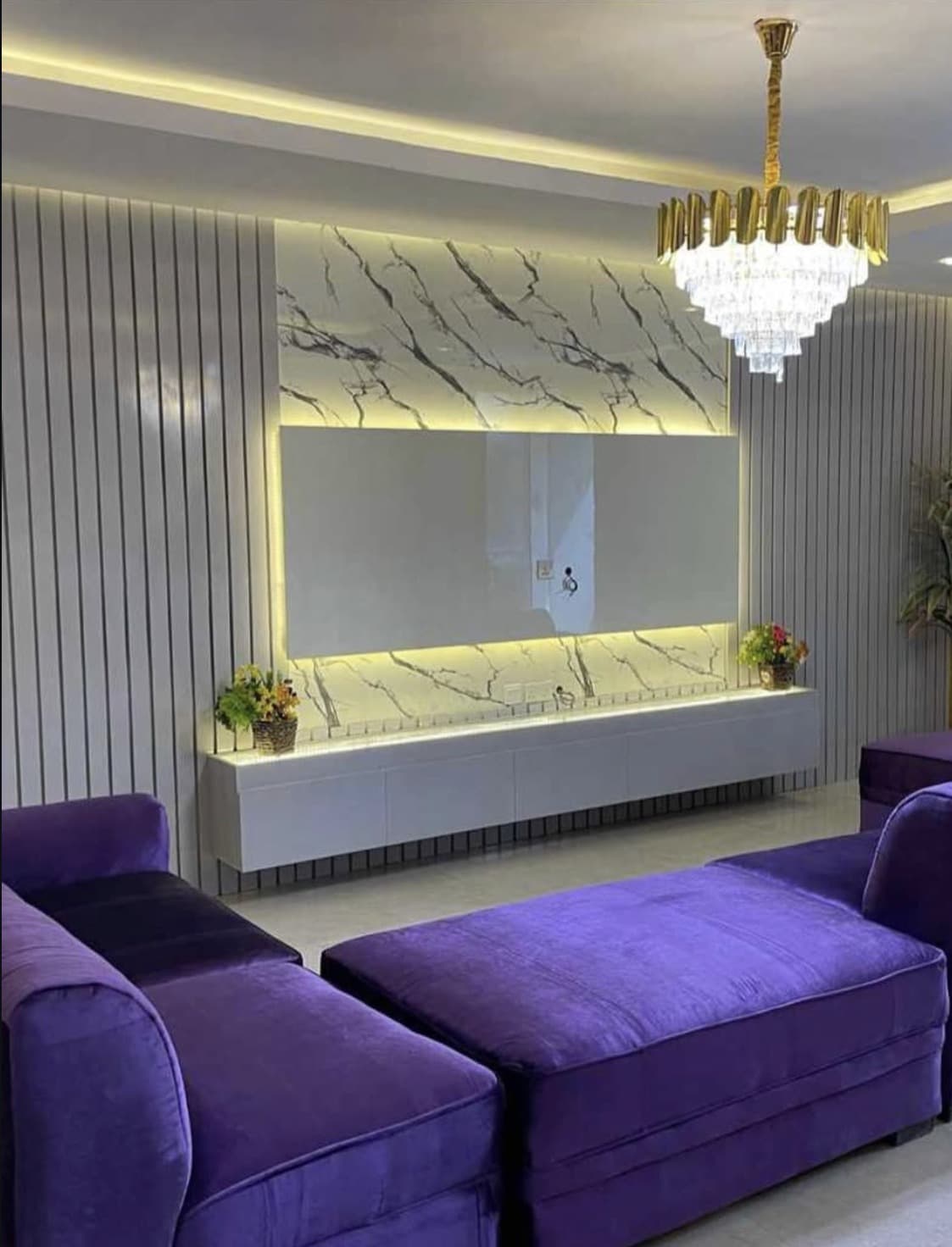 A living room with a marble feature wall, gold chandelier and velvet seating